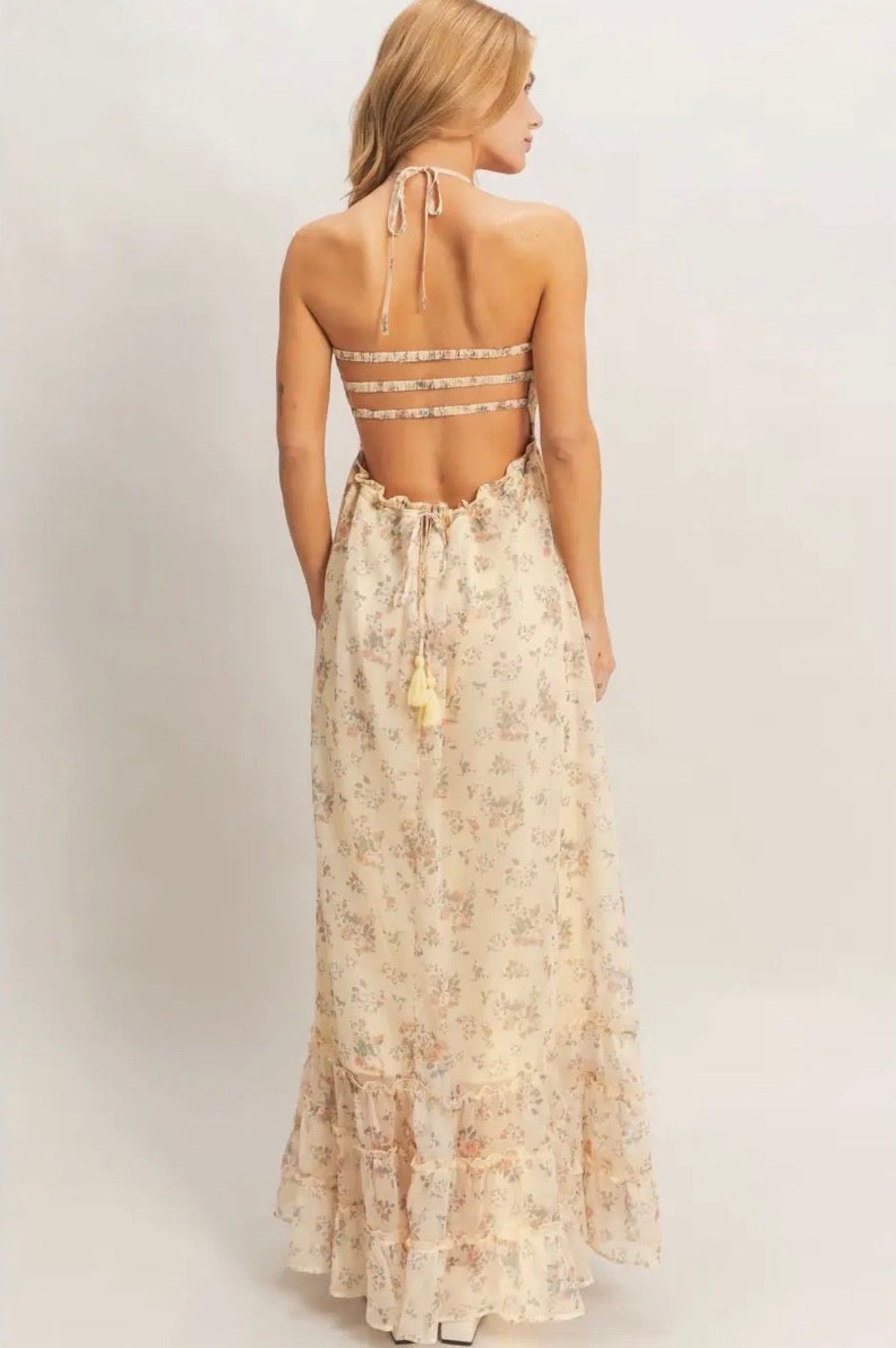 Woman wearing a floral dress with an open back on a plain background