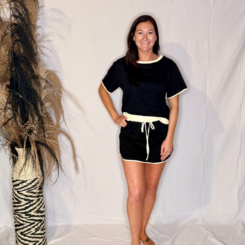 Woman wearing a black outfit with white trim standing against a plain background