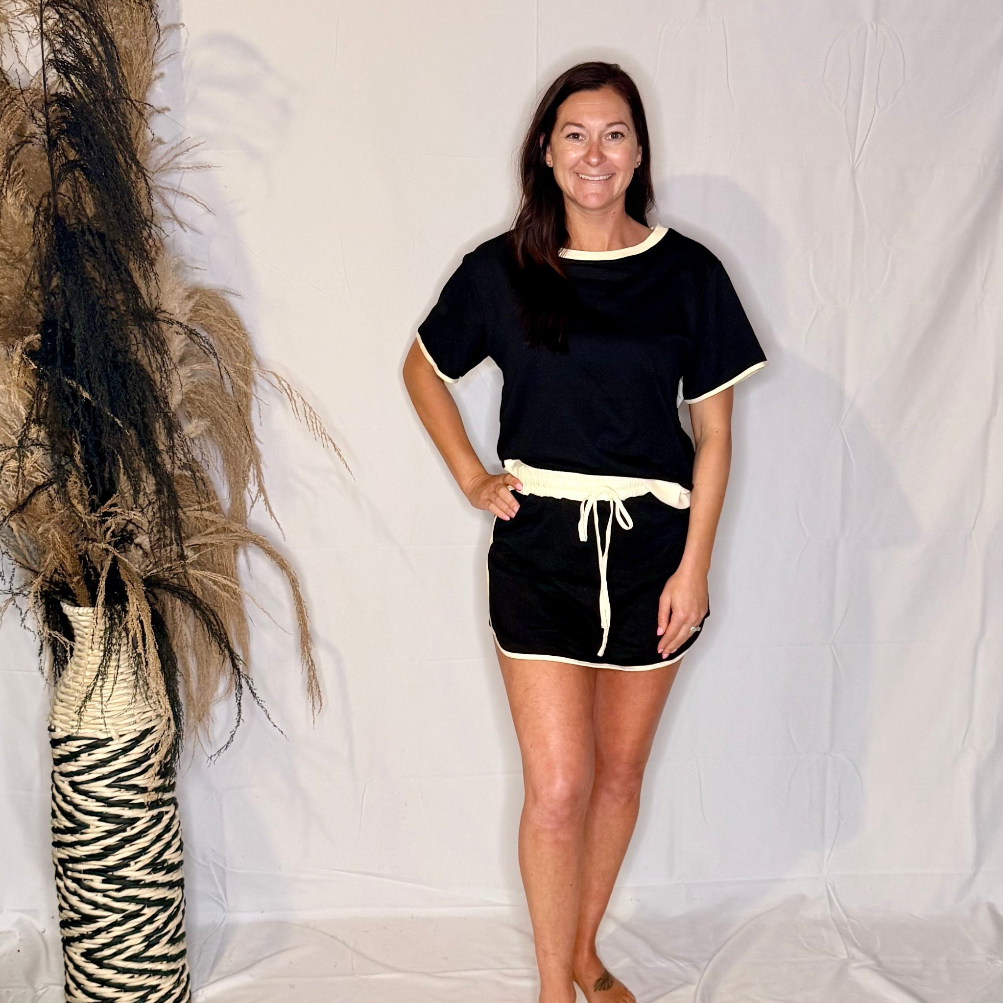 Woman wearing a black outfit with white trim standing against a plain background