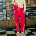 A woman stands in a record store wearing a cream knit sweater with a red horse graphic and bright red drawstring pants with patterned side trim, paired with red sneakers.