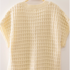 A cream-colored textured knit short-sleeve top hanging on a wooden hanger with the brand name 'VERY J' visible, set against a plain off-white background.