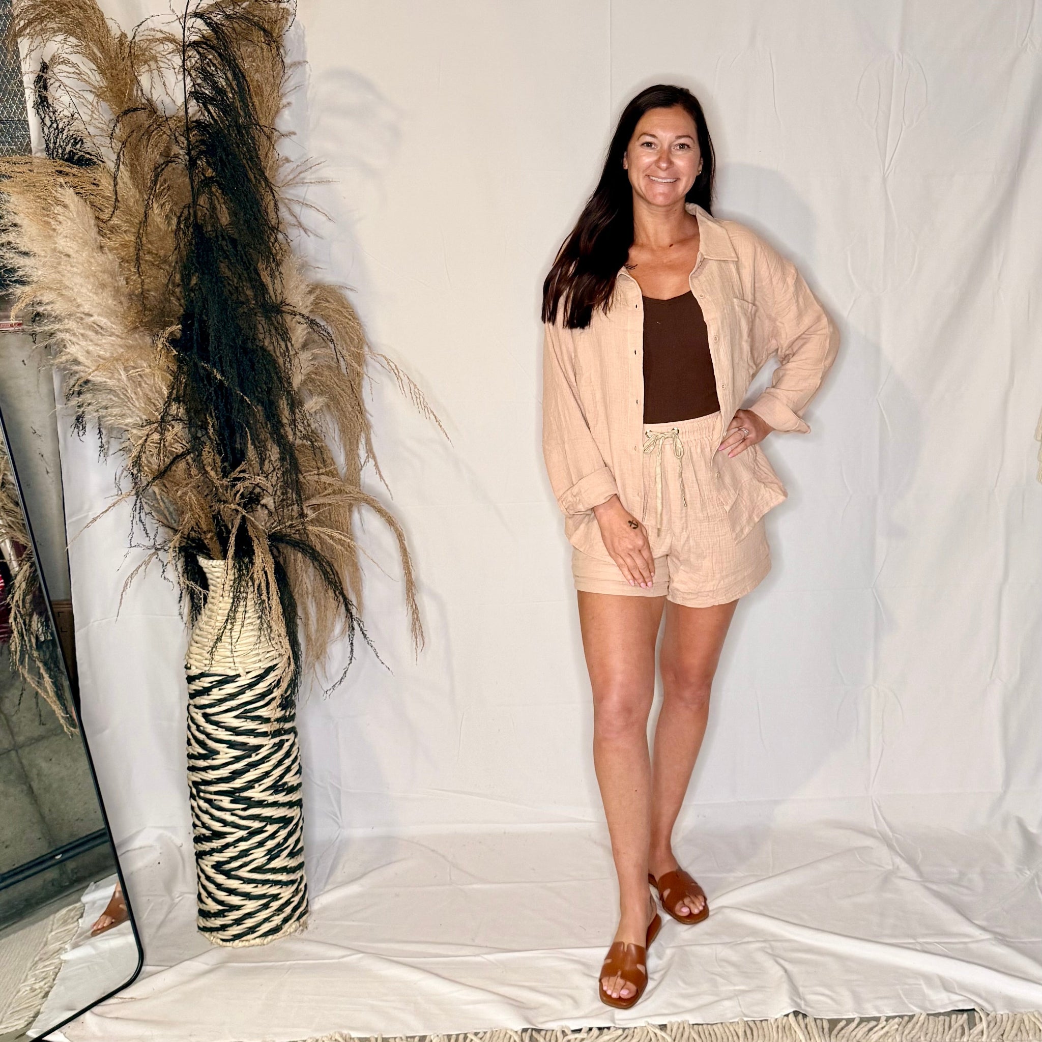 Woman in a beige outfit standing next to decorative pampas grass and a zebra-striped vase on a white background