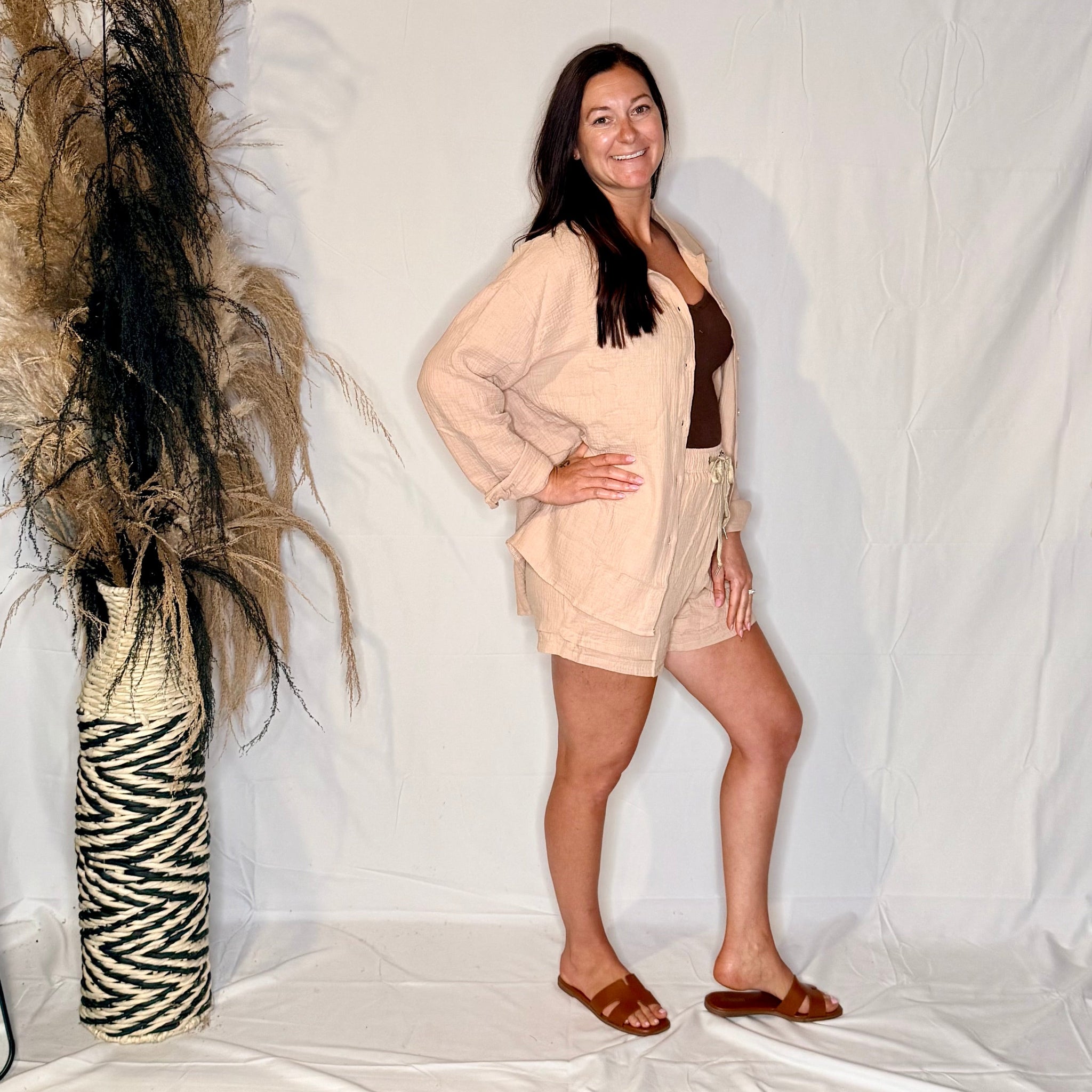 Woman in a beige outfit standing in front of a white backdrop with decorative elements.