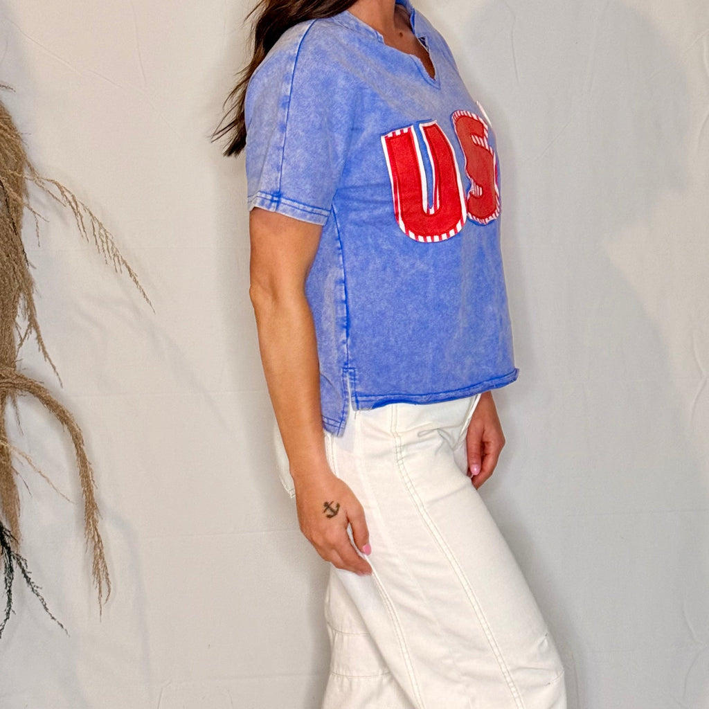 Person wearing a blue denim shirt with red lettering and white pants against a neutral background