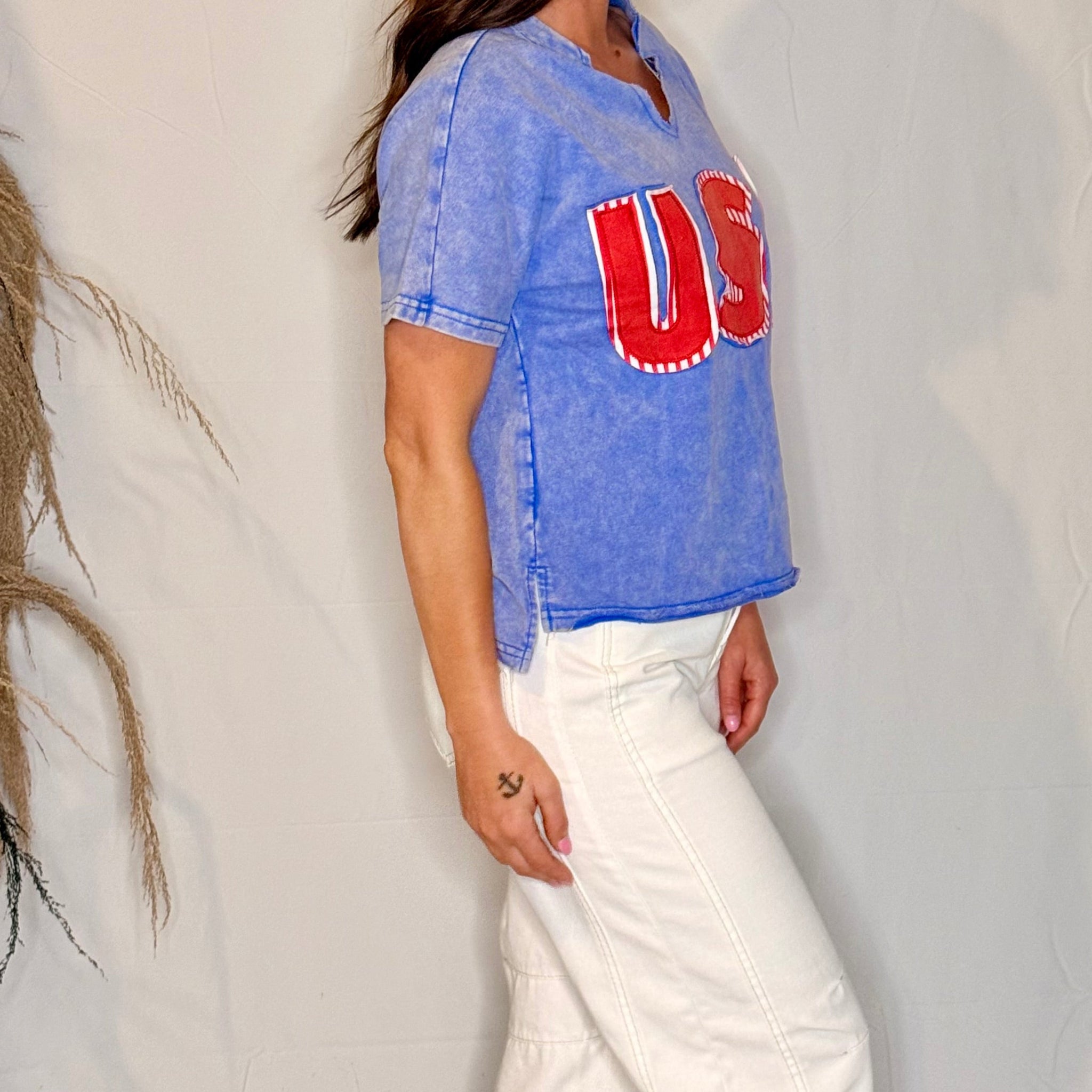 Person wearing a blue denim shirt with red lettering and white pants against a neutral background