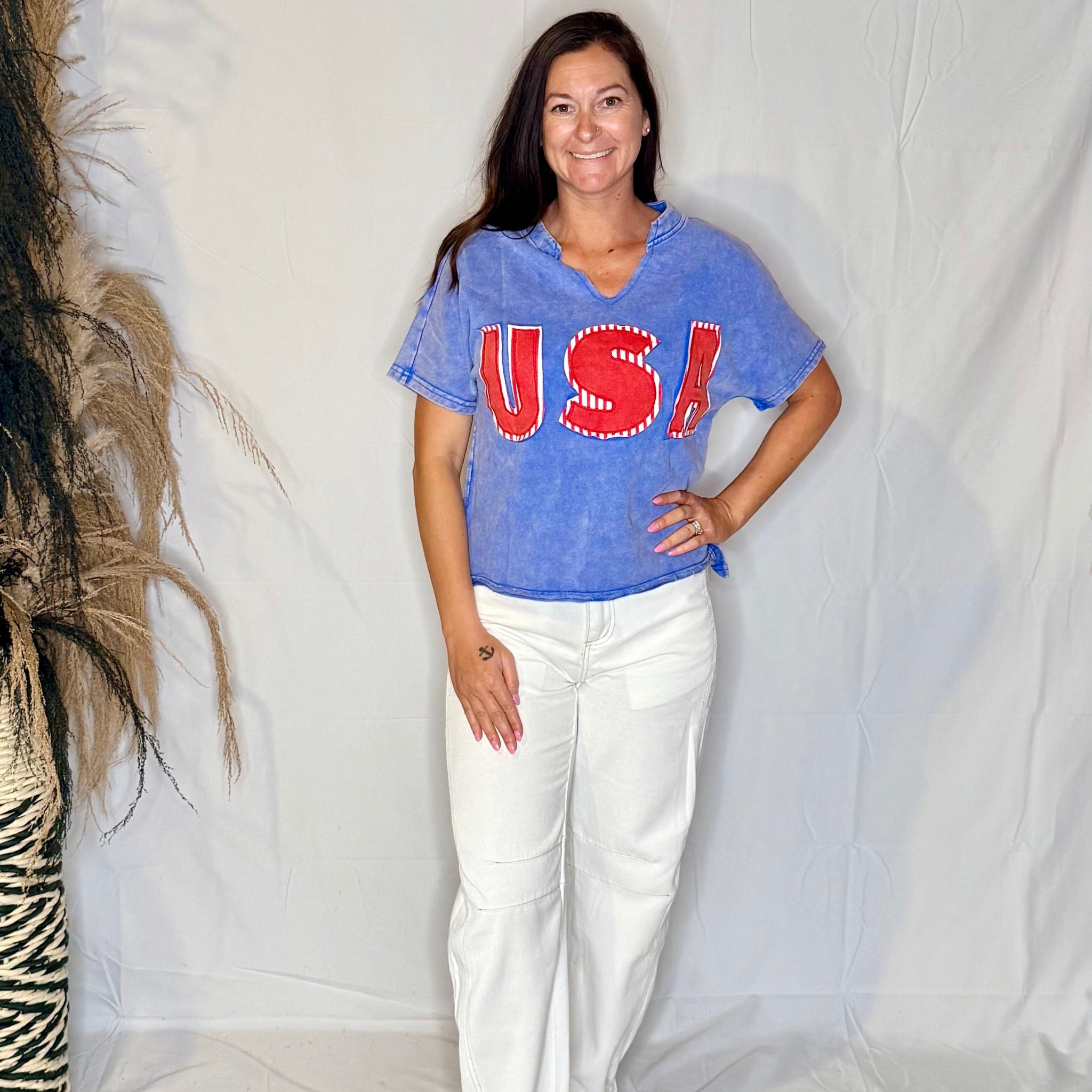 Woman wearing a blue 'USA' t-shirt and white pants against a plain background
