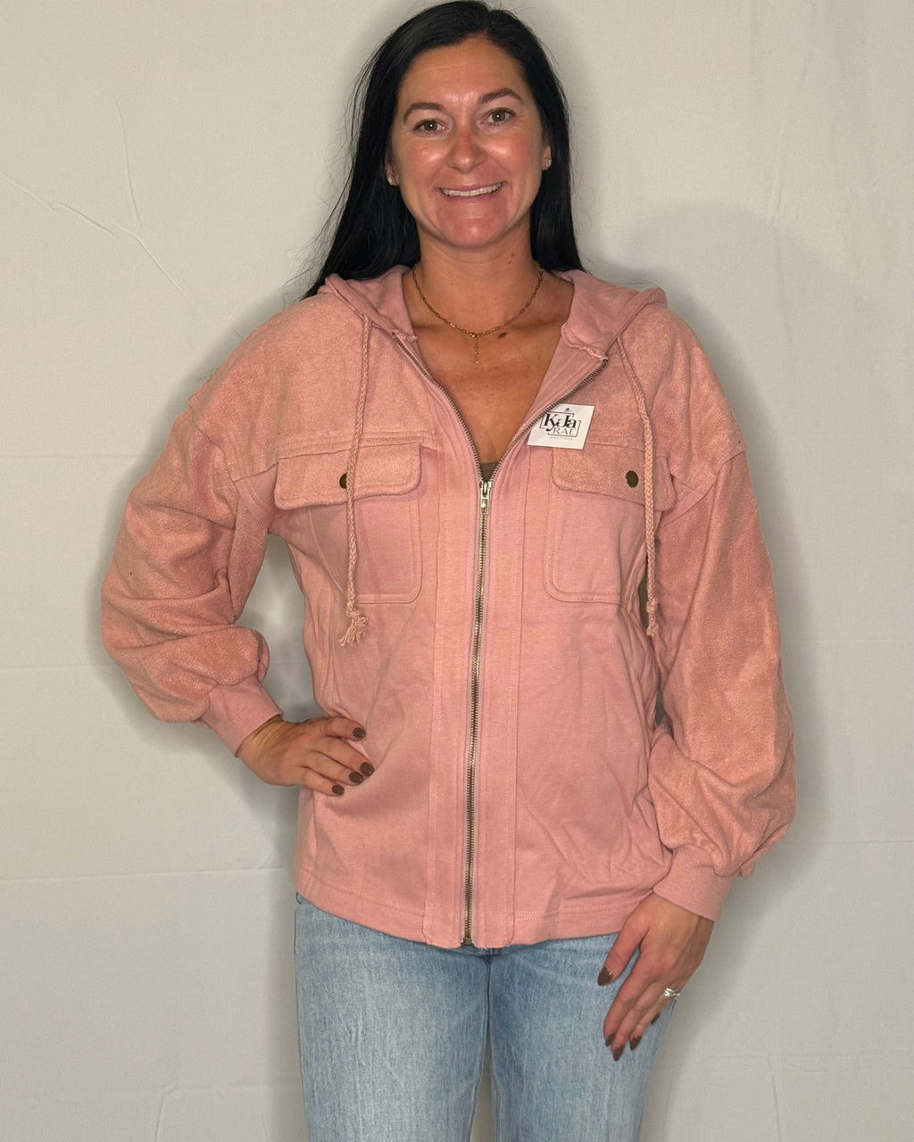 Woman wearing a pink jacket with a brand tag against a plain background